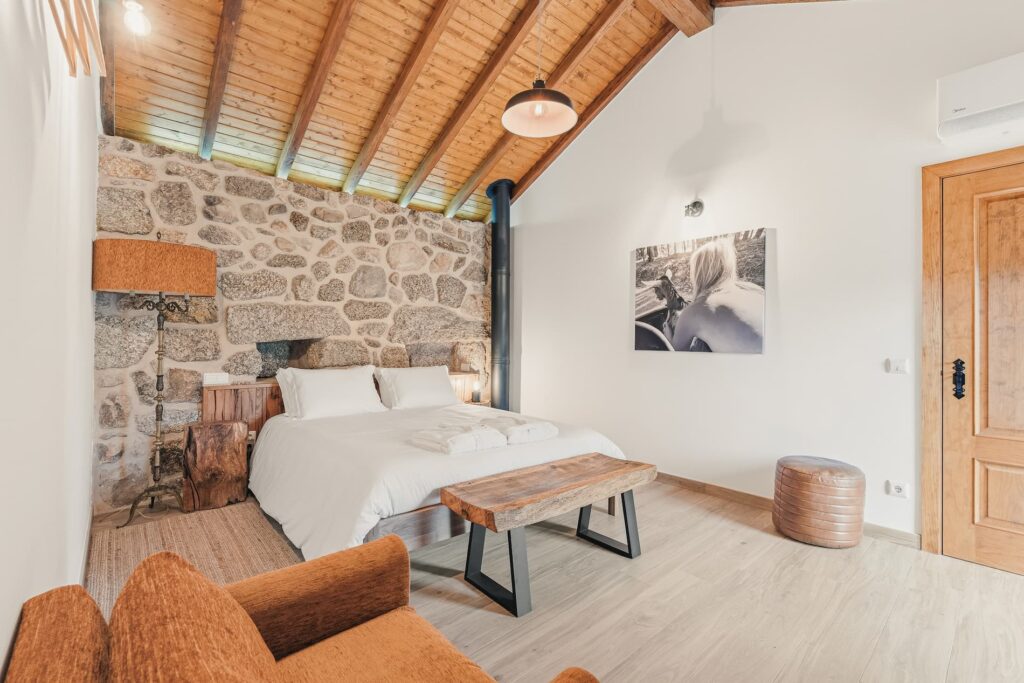 Banduja Casa das Cabras: quarto com parede de pedra, teto de madeira e cadeirao laranja