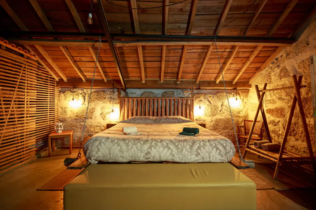 Quarto rustico com cama suspensa por correntes, paredes de pedra e luz quente