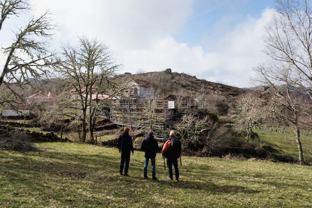 Três pessoas a caminhar no terreno do Fundo da Aldeia, com a aldeia ao fundo